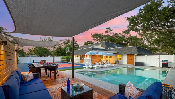 A pool area with lounge chairs, a dining table, and a covered seating area.