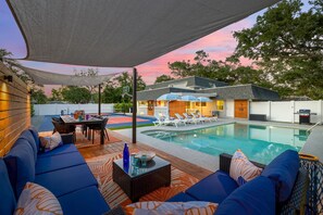 Zona de piscina con sillas de descanso, una mesa de comedor y un área de estar techada.