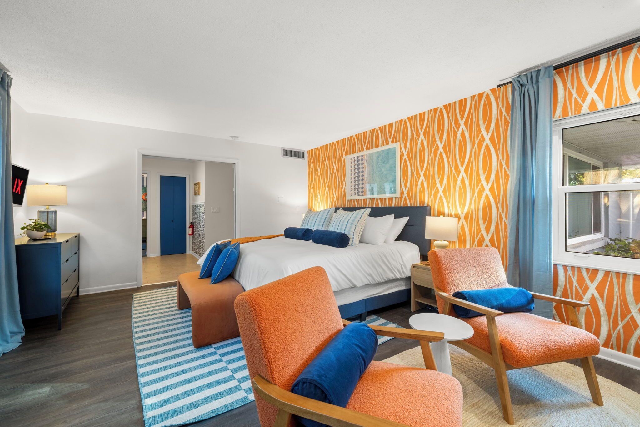 Una habitación de hotel moderna con una cama grande, dos sillones, una mesita y una ventana con vistas.