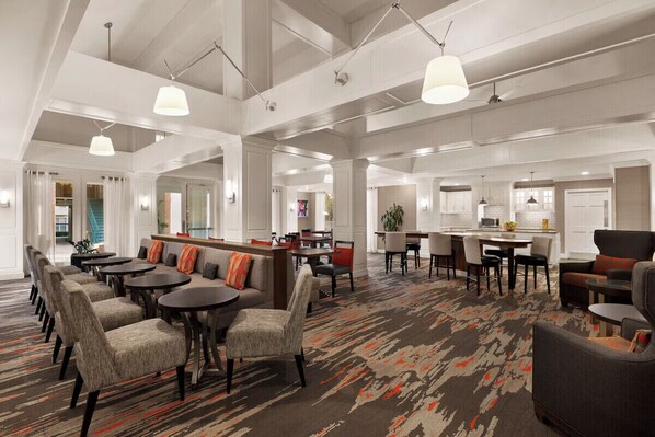Un amplio hall de hotel con varias zonas de estar, un bar y una cocina a la vista.