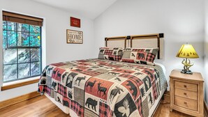 Um quarto com uma cama grande, uma mesa de cabeceira, um abajur, uma janela com vista para árvores e um ventilador de teto.