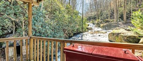 Una terraza de madera con un enfriador de hielo con la marca Coca-Cola, con vistas a una zona boscosa con un arroyo.