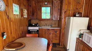 Ein Holzblockhaus-Interieur mit einem runden Esstisch, einem Herd, einem Spülbecken und einem Kühlschrank.