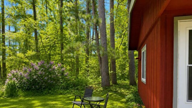 Ein rotes Gebäude mit einer weißen Tür, umgeben von einem gepflegten Garten mit Tisch und Stühlen.