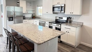 Eine moderne Küche mit weißen Schränken, Granit Arbeitsplatten, Edelstahlgeräten und einer zentralen Kochinsel mit Barhocker.