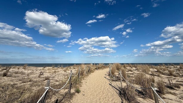 Ein Sandweg am Strand, mit blauem Himmel und weiter Ferne.