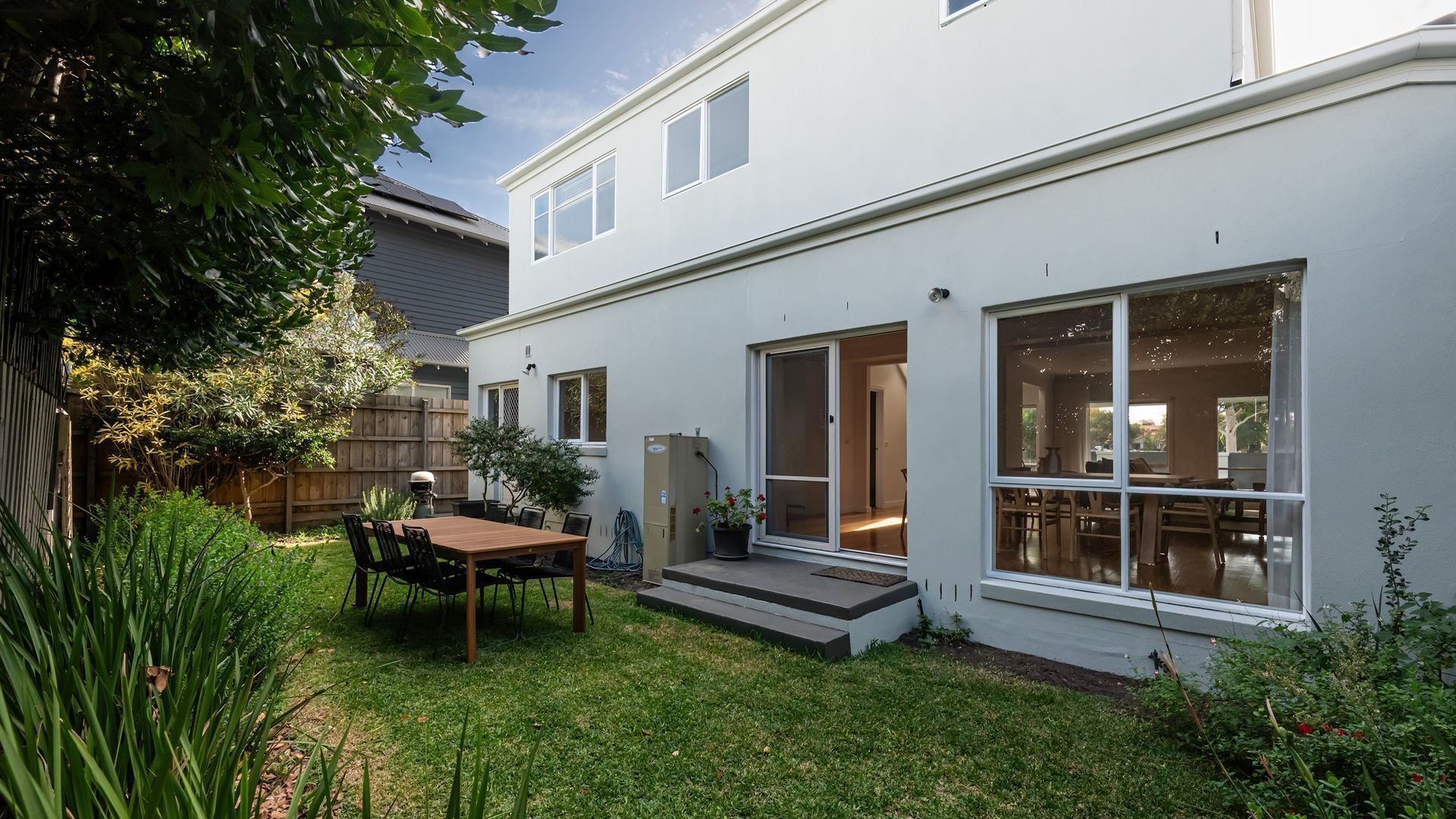 A modern two-story house with a patio, a dining area, and a large sliding glass door leading to an interior space.