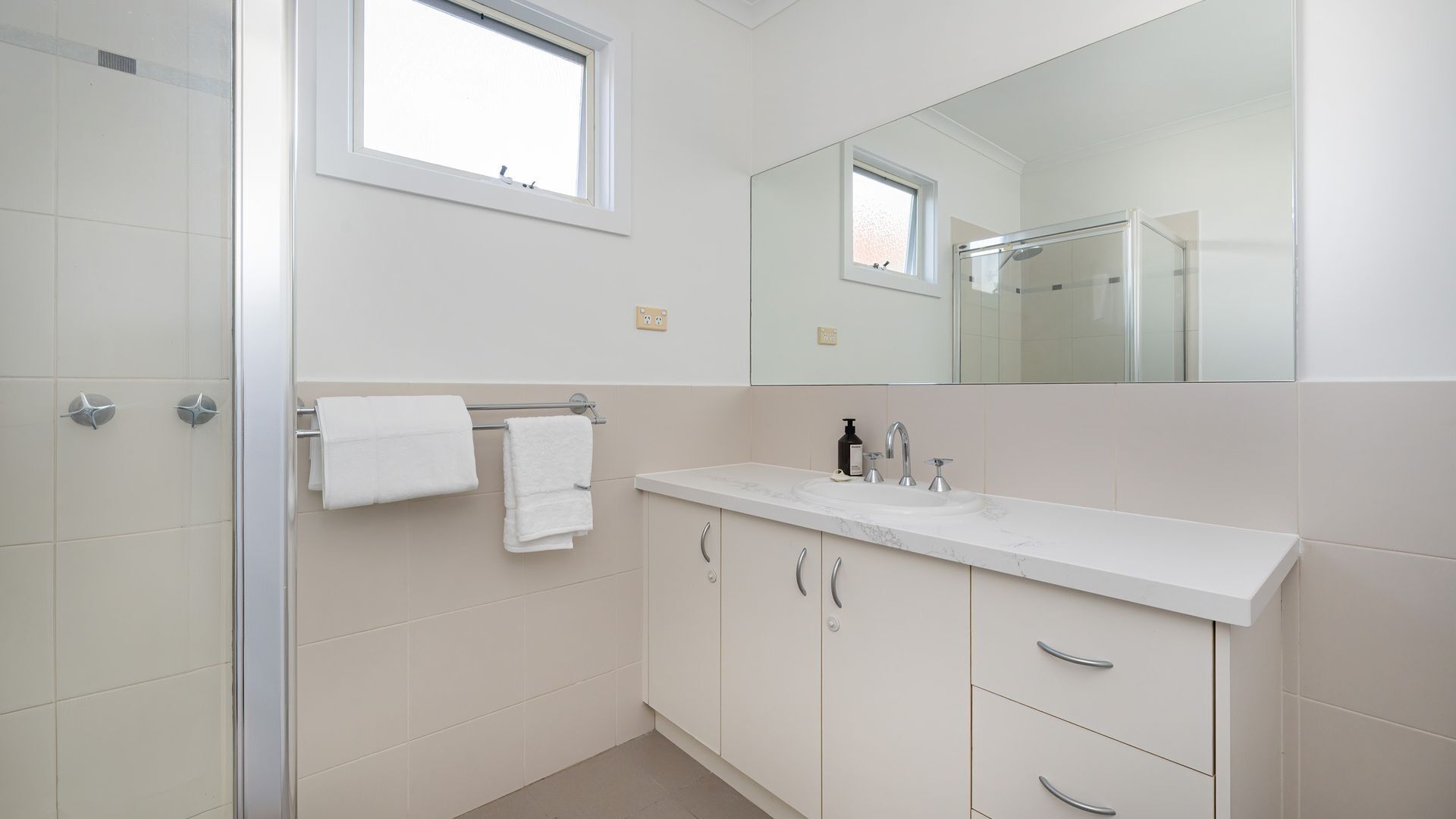 A modern bathroom with a glass shower enclosure, a white sink with a marble countertop, and a large mirror above the sink.