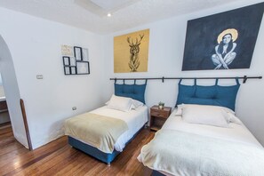 Une chambre avec deux lits, un plancher en bois et des œuvres d’art accrochées aux murs.