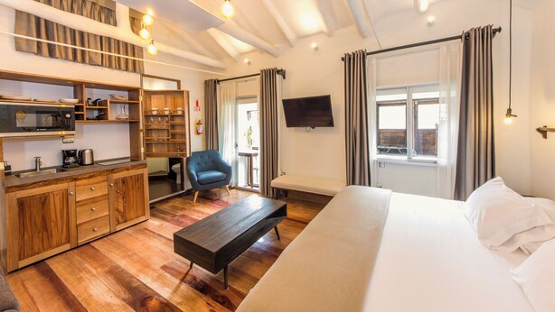 Een moderne hotelkamer met een houten kitchenette, een groot bed, een bankje en een aan de muur bevestigde televisie.