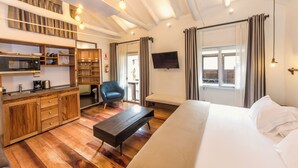 Una habitación de hotel moderna con una kitchenette de madera, una cama grande, un banco y un televisor montado en la pared.