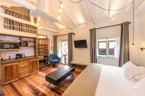 Une chambre d’hôtel moderne avec une kitchenette en bois, un grand lit, un banc et un téléviseur fixé au mur.