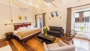Una habitación de hotel moderna con una cama grande, un sofá, una mesa de centro y una silla. Tiene un balcón con vistas.
