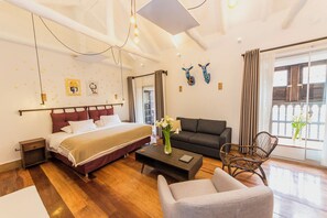 Une chambre d’hôtel moderne avec un grand lit, un canapé, une table basse et un fauteuil. Elle dispose d’un balcon avec vue.