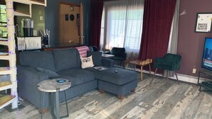 A living room with a sectional sofa, a small table, a chessboard, and a TV. - Charming Red Tower, Loft  ambiance, Mountain views, AC, WiFi, Berkshires NY (Petersburgh)