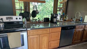 A modern kitchen with stainless steel appliances, wooden cabinets, and a large window offering a view of trees. - Charming Red Tower, Loft  ambiance, Mountain views, AC, WiFi, Berkshires NY (Petersburgh)