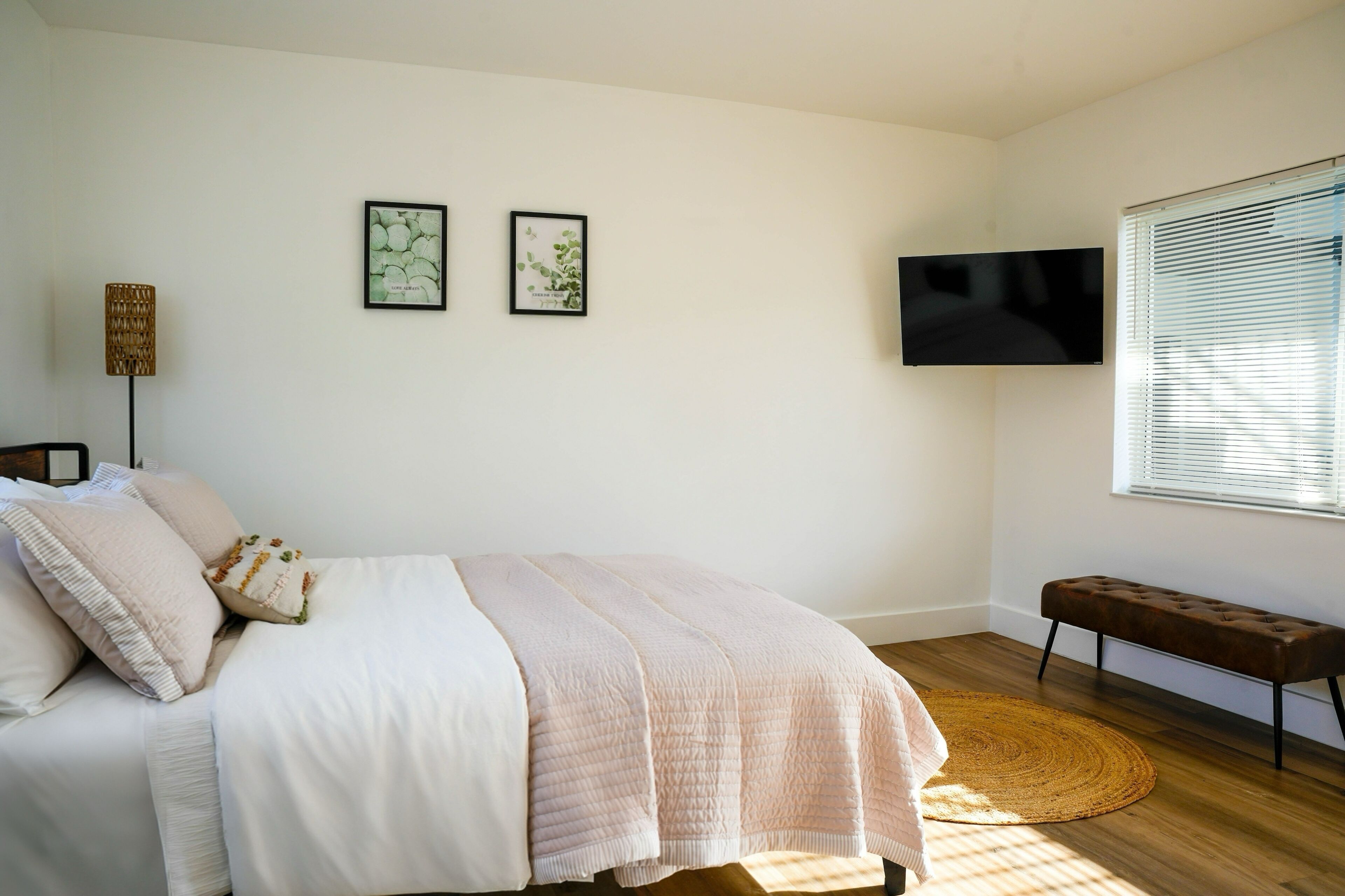 A bedroom with a bed, a bench, a TV, and two framed pictures on the wall.