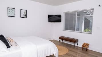 A bedroom with a bed, a television, a bench, and a window with blinds.