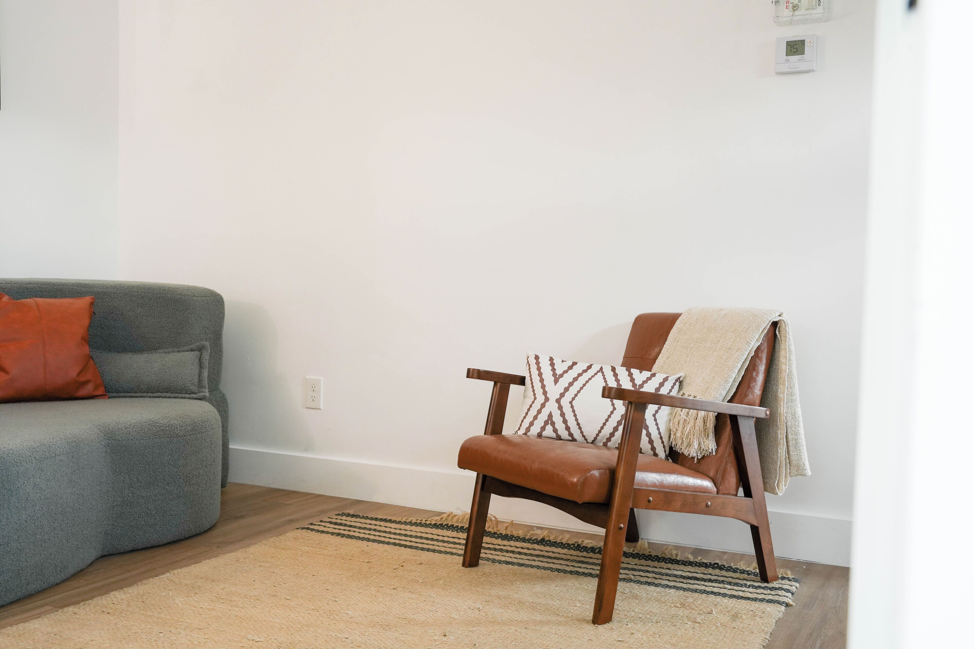 Una sala de estar con un sofá gris, un sillón de cuero marrón y un plaid estampado sobre el sillón.