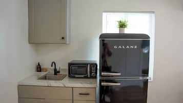 Eine Küche mit einem schwarzen Galanz-Kühlschrank, einer Mikrowelle und einem Waschbecken mit Marmorarbeitsplatte.