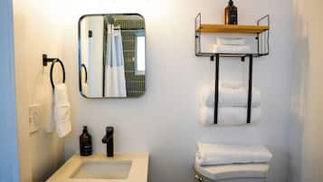 Un baño con lavamanos, espejo, toallero y repisas con artículos de tocador.