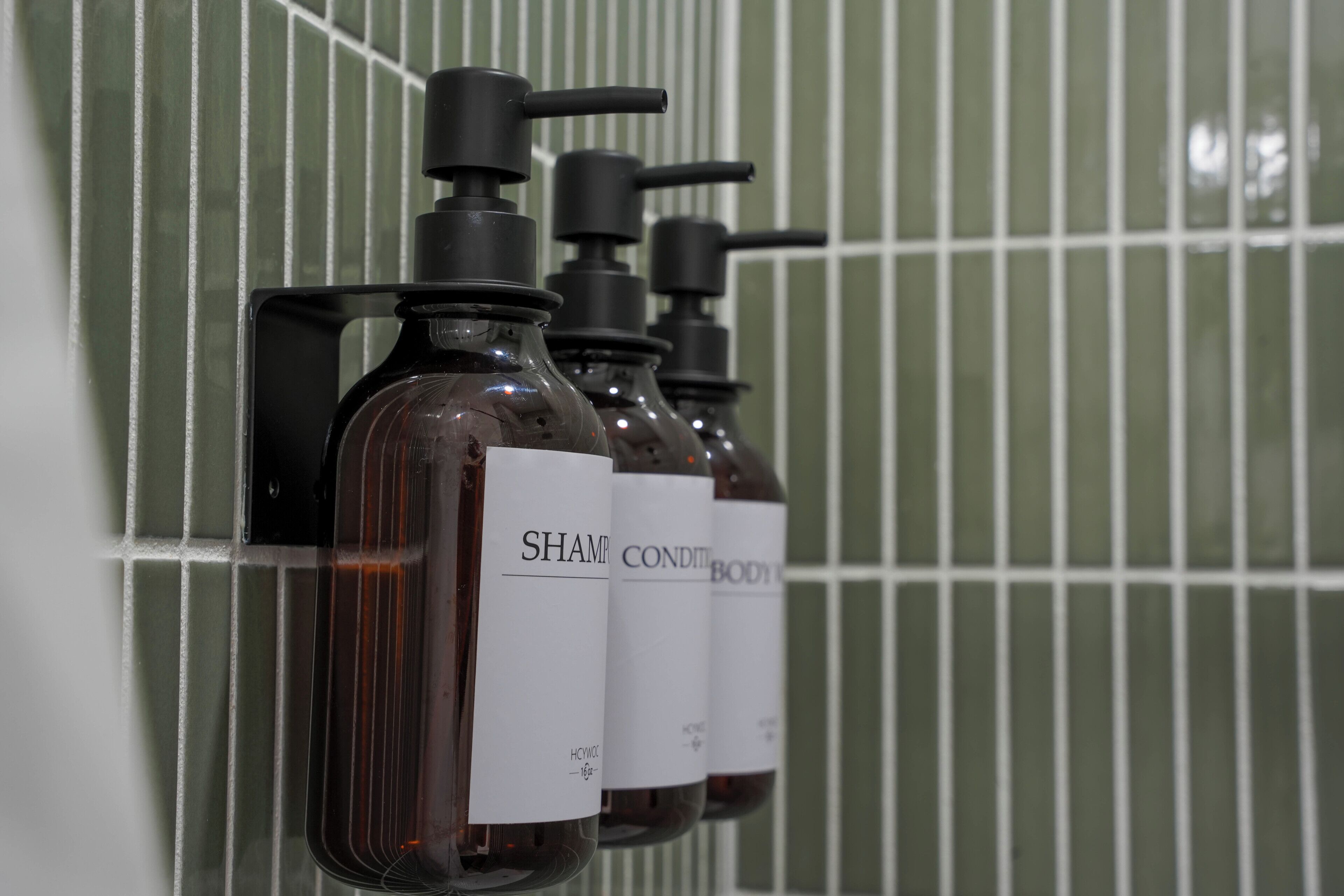 Tre flaconi di shampoo e balsamo su un muro piastrellato.