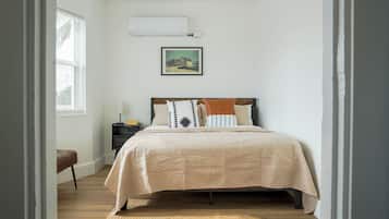 Une chambre à coucher avec un lit, une table de chevet, une lampe, un tableau au mur et une fenêtre avec des stores.