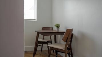 Un comedor con una mesa de madera y cuatro sillas, una planta en maceta sobre la mesa y una ventana con persianas.