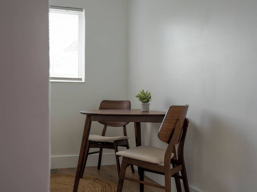 Un comedor con una mesa de madera y cuatro sillas, una planta en maceta sobre la mesa y una ventana con persianas.