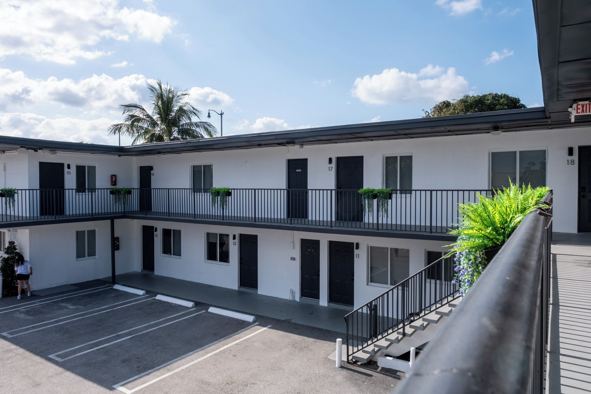 Un motel de dos pisos con puertas numeradas, un estacionamiento y una escalera que lleva al piso superior.