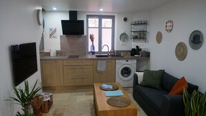 A compact living space with a kitchenette, a washing machine, a sofa, and a coffee table. - Cosy studio in the heart of the village of Chazay (Chazay-d'Azergues)