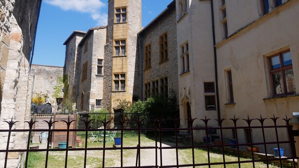 A courtyard with stone buildings, a tower, and a metal fence. - Cosy studio in the heart of the village of Chazay (Chazay-d'Azergues)
