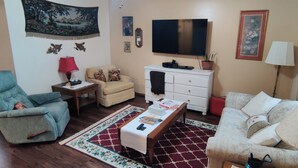 Ein Wohnzimmer mit Sofa, Sessel, Couchtisch, Fernseher und Kamin.