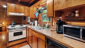 A wooden cabin kitchen with a stove, sink, and microwave.