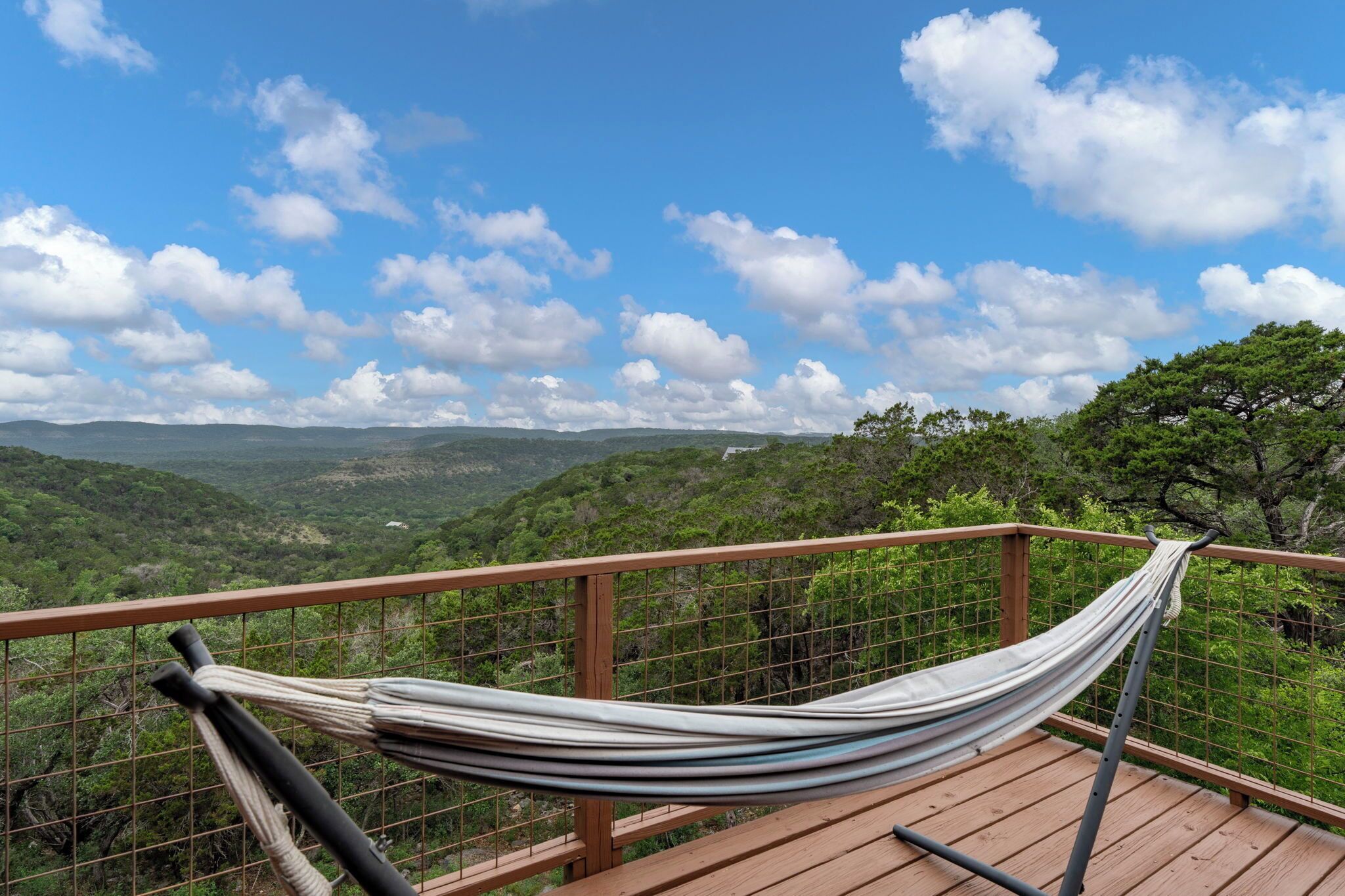 Un hamac sur une terrasse en bois, offrant une vue sur un paysage montagneux sous un ciel dégagé.