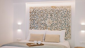 Een netjes opgemaakt bed met een decoratief hoofdbord, een nachtkastje met een dienblad en een klein houten krukje.