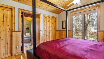 A bedroom with wooden walls, a ceiling fan, a large window, and a bed with a red bedspread.