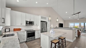 A modern kitchen with white cabinets, stainless steel appliances, a granite countertop, and a large island with bar stools.