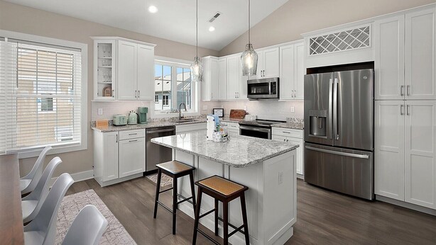 A modern kitchen with white cabinetry, stainless steel appliances, a granite countertop, and a central island with bar stools.