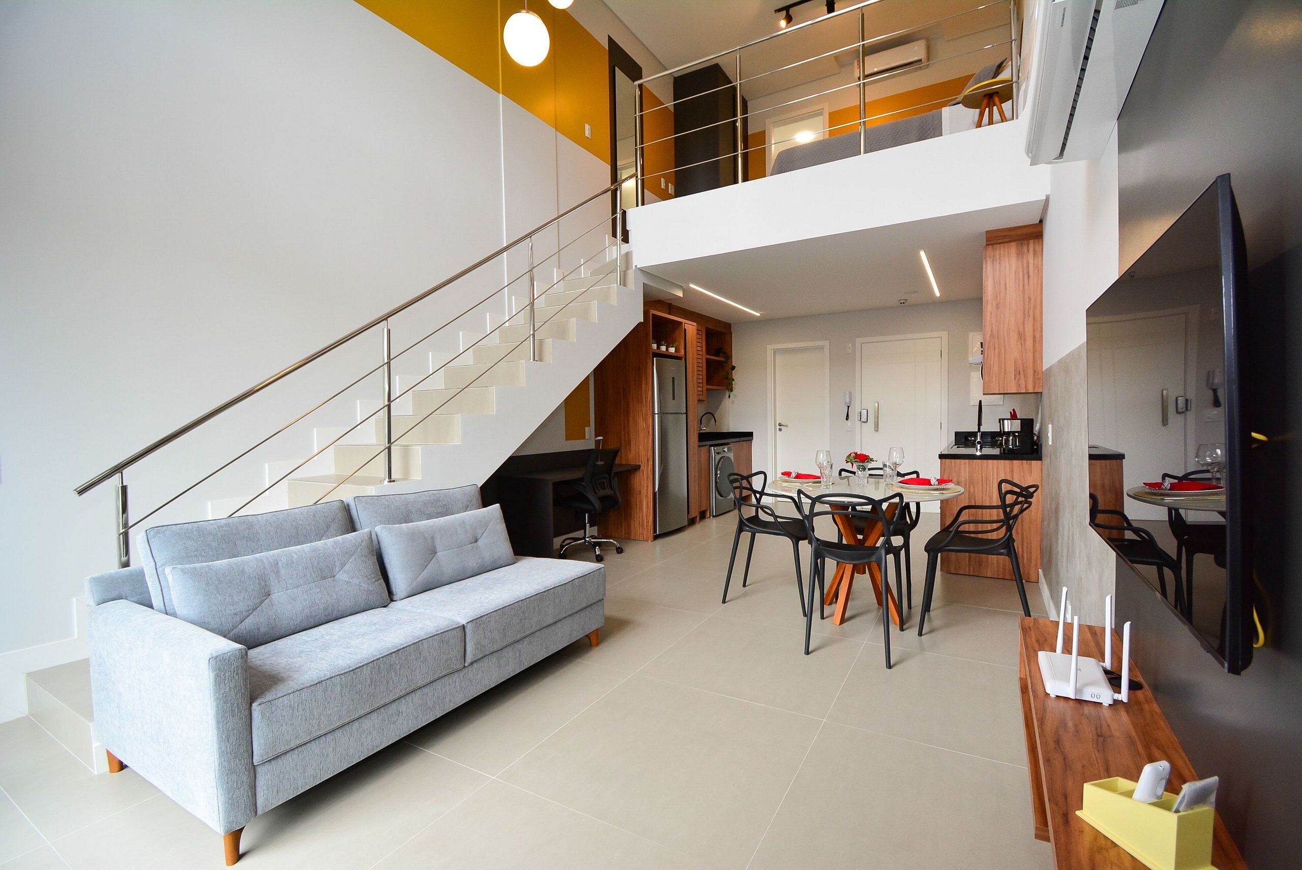 Un apartamento moderno con un sofá gris, comedor, cocina y una escalera.