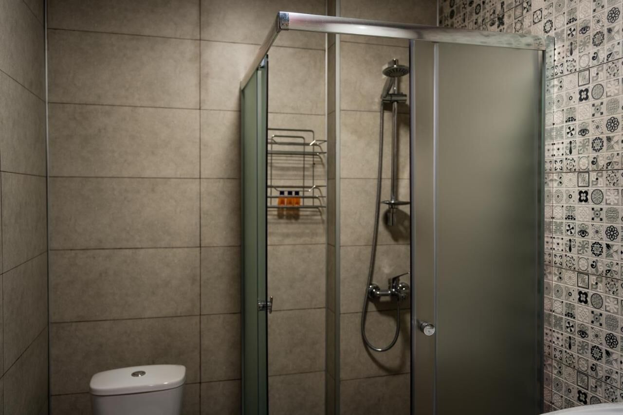 Une salle de bain dotée d’une douche à parois de verre, de toilettes et d’un mur carrelé orné d’un motif décoratif.