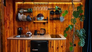 A compact kitchen with wooden walls, a sink, a black refrigerator, and shelves holding dishes and glasses. - Greenland Pheria - Cabin near Batumi (Batumi)