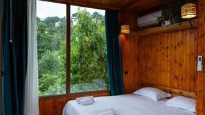 A wooden-paneled room with a large window, a bed with white linens, and a wall-mounted air conditioning unit. - Greenland Pheria - Cabin near Batumi (Batumi)