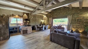 A rustic interior with exposed wooden beams, a stone wall, a kitchen area, and a seating area with a sofa and chairs.