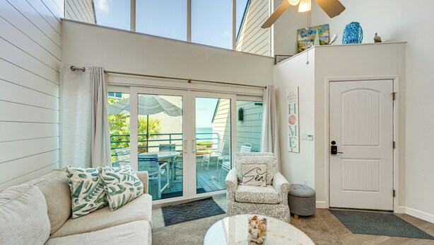 A room with a sofa, armchair, and round table, a door, and a view through a glass door to an outdoor area with chairs and a table. - Beachfront Condo w/ Balcony on Manasota Key (Englewood)
