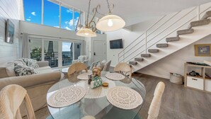 A modern living room with a glass dining table, beige sofas, and a staircase leading to an upper level. - Beachfront Condo w/ Balcony on Manasota Key (Englewood)