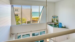 A room with a large window overlooking a beach, a staircase, and a small table with decorative items. - Beachfront Condo w/ Balcony on Manasota Key (Englewood)