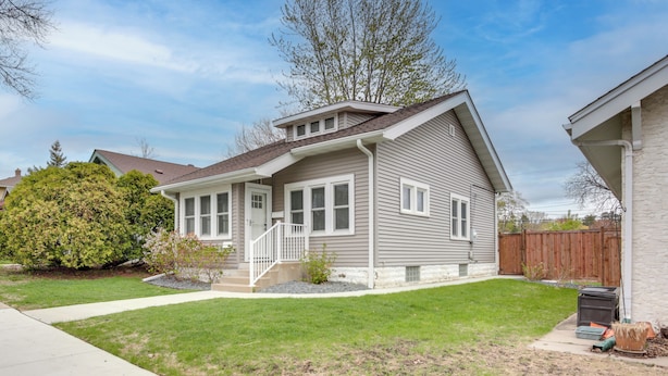 A two-story house with a front porch, a small front yard, and a wooden fence in the background. - Cozy Minneapolis Retreat: Walk to Shops & Eats (Minneapolis)
