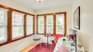 A room with large windows, a desk with a computer, a chair, and a small table with a lamp. - Cozy Minneapolis Retreat: Walk to Shops & Eats (Minneapolis)