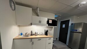 Kompakti keittiö, jossa on työtasolla mikroaaltouuni, leivänpaahdin ja kahvinkeitin, sekä jääkaappi ja seinällä oleva kello.